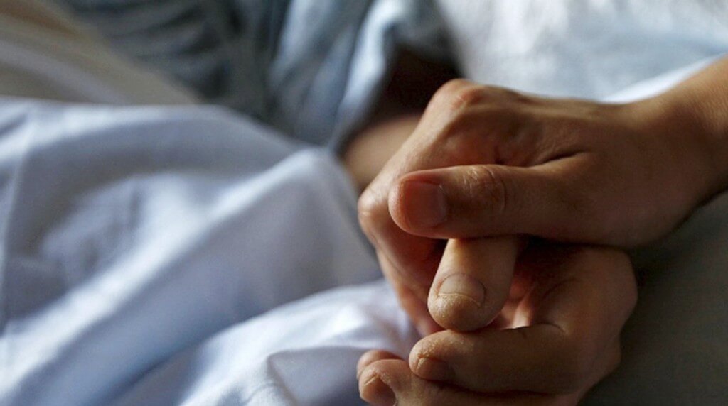 Persona sujetando la mano de un enfermo en una camilla de hospital.